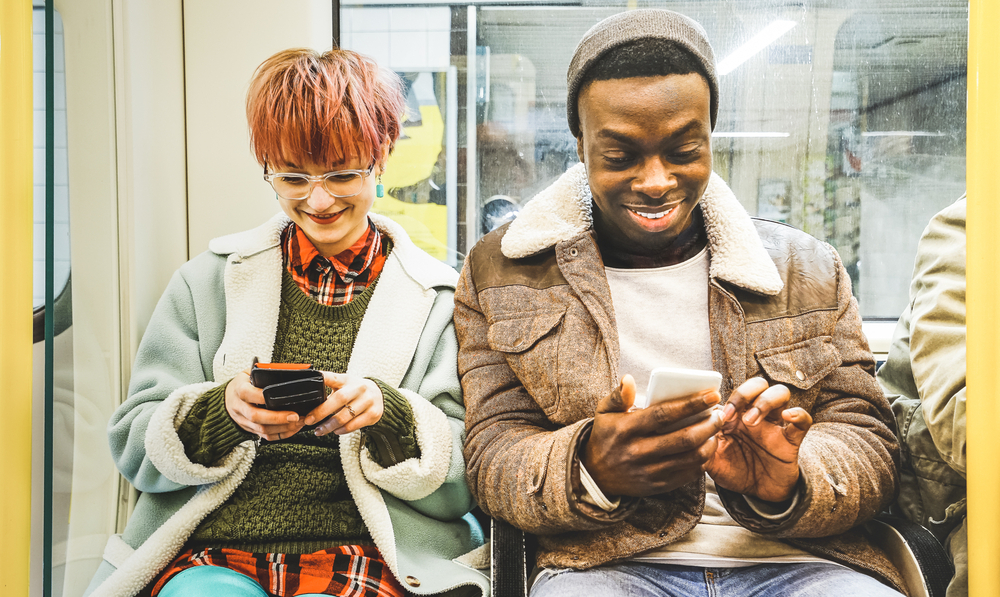 Un homme et une femme sourient en regardant leurs téléphones dans le métro de Londres