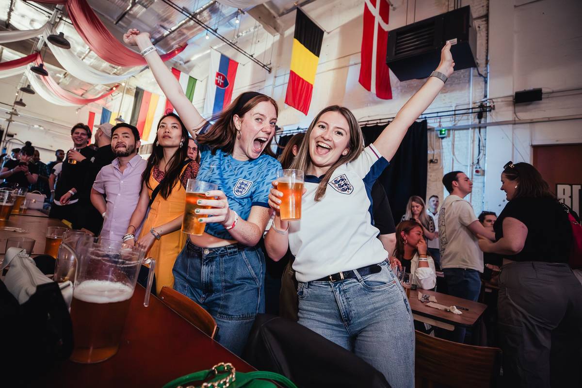 supporters at a football screening in a big beer hall cheering with beers in hand
