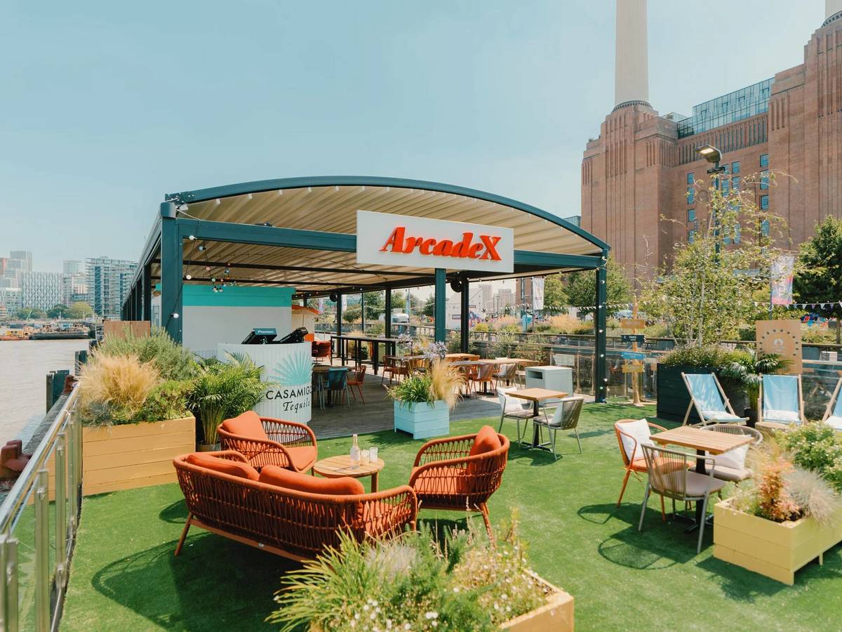 chairs and tables scattered around the al fresco floating food hall 'arcade x' with battersea power station visible in the background