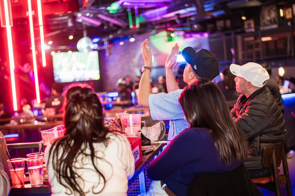 fans cheering at a sports screening in a neon drenched room at a sports bar