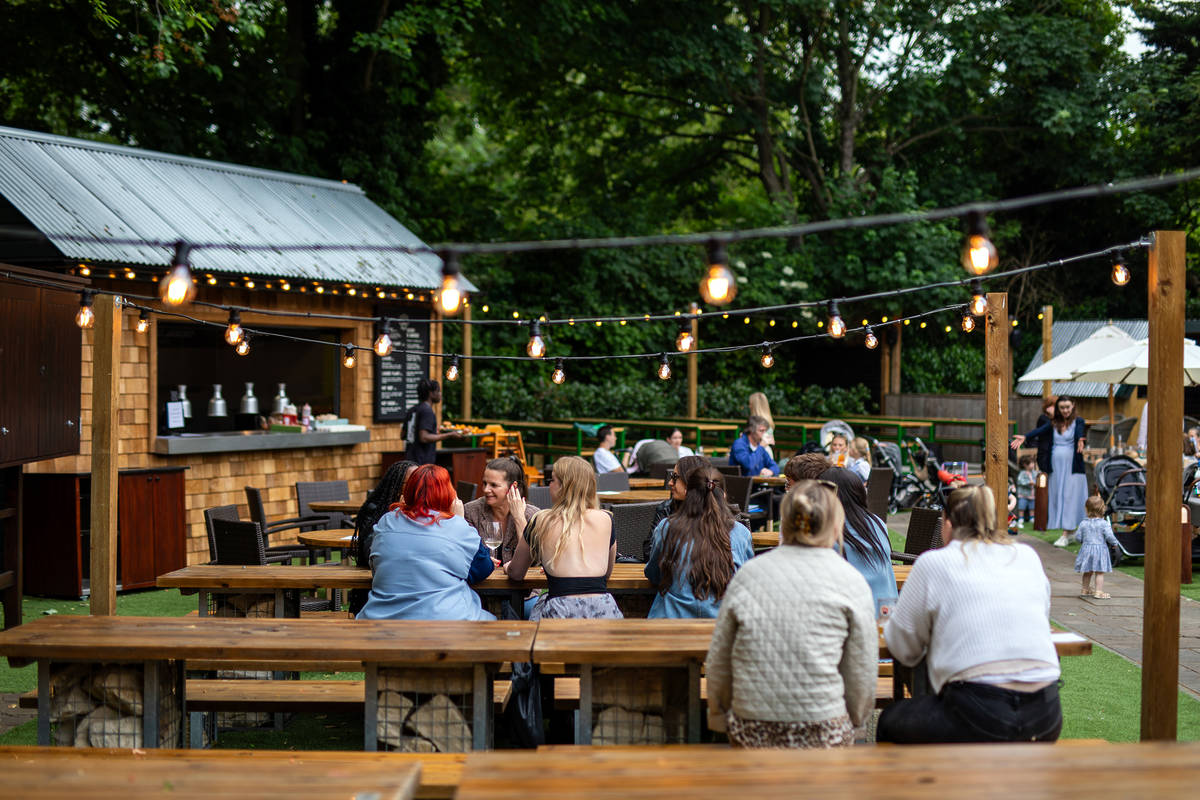 people sat at tables in a beer garden under charming fairy lights