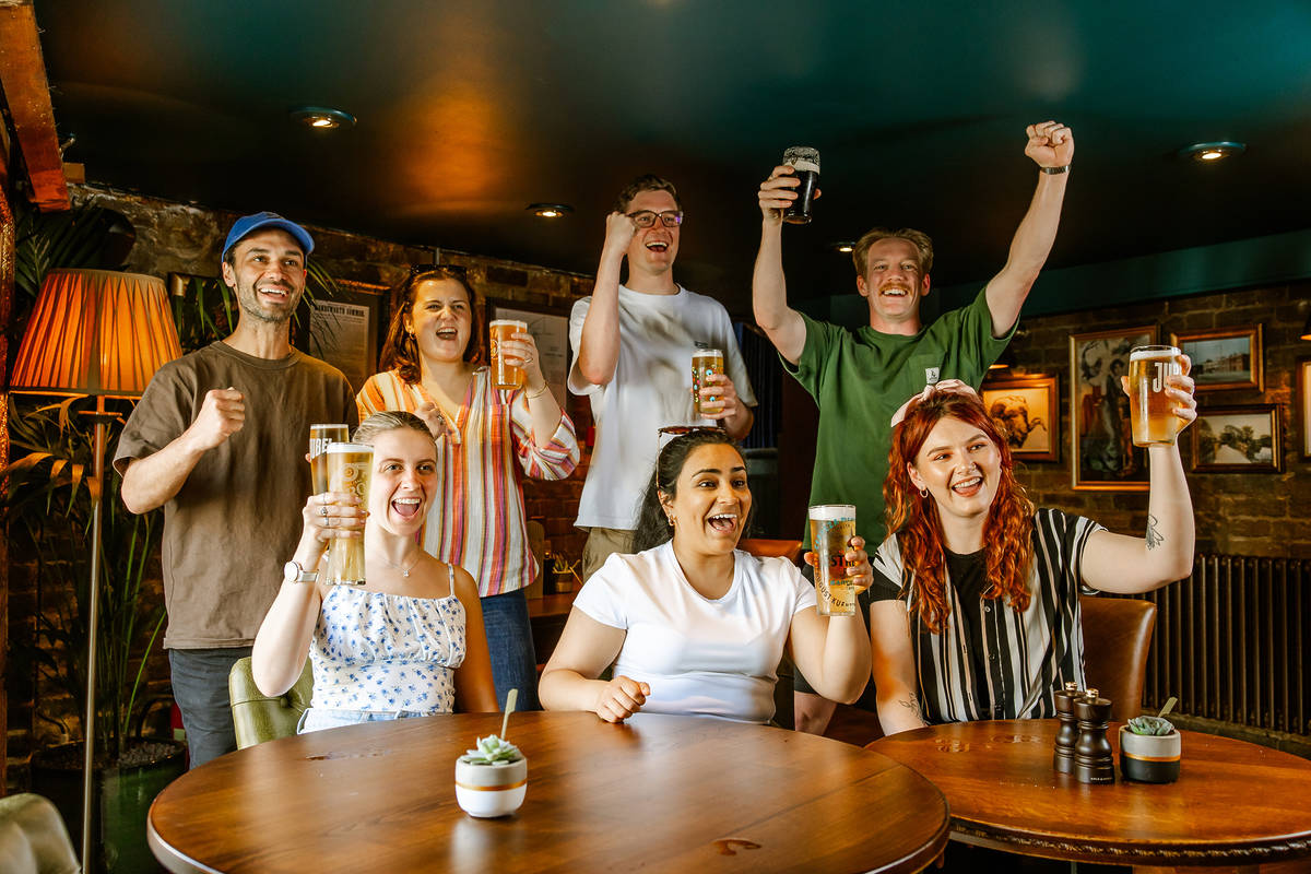 People standing and sitting around a table cheering as they watch a sporting fixture
