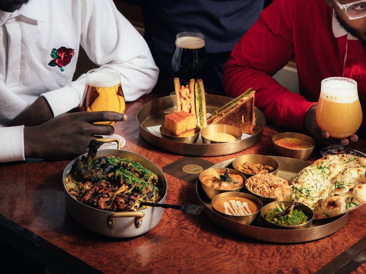 two people in jerseys sitting at a table with an indian bbq feast and glasses of beer in front of them