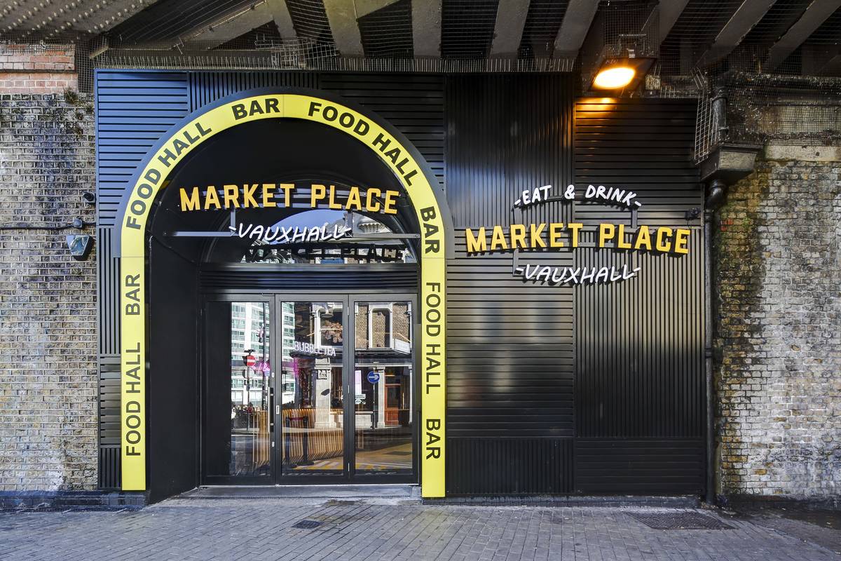 the yellow framed entrance to market place vauxhall, underneath a railway arch