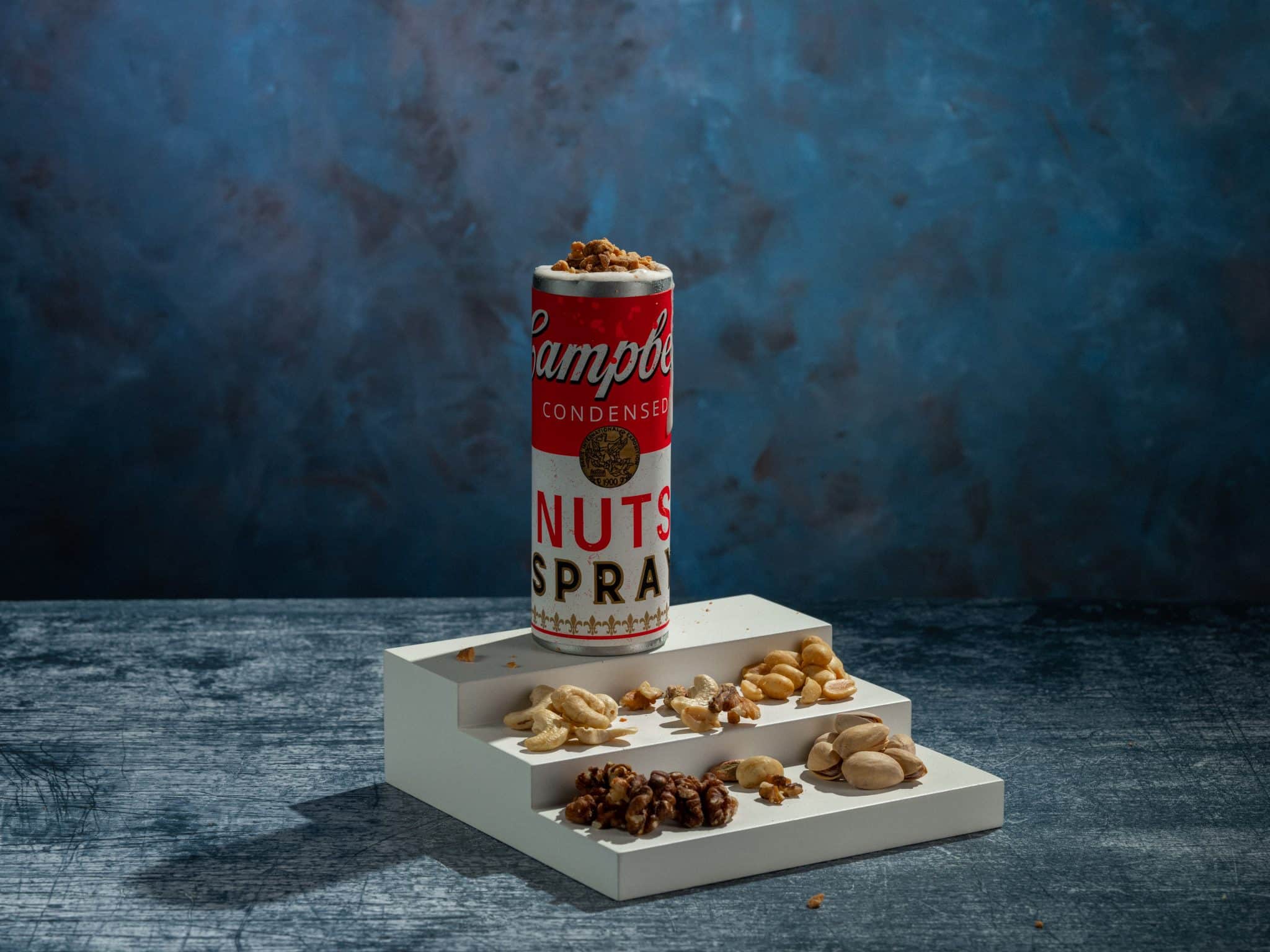 A repurposed Campbell's soup can serving as a cocktail glass, on some steps that are covered in assorted nuts.