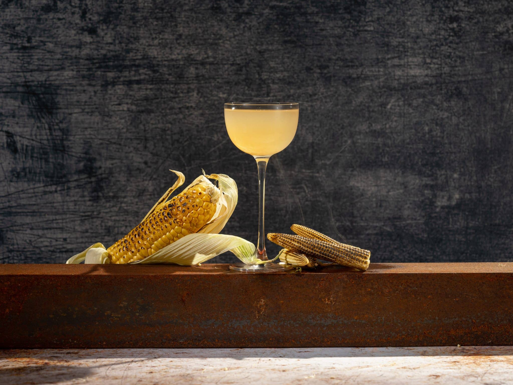 Some corn next to a coupe glass holding the CornBread! cocktail