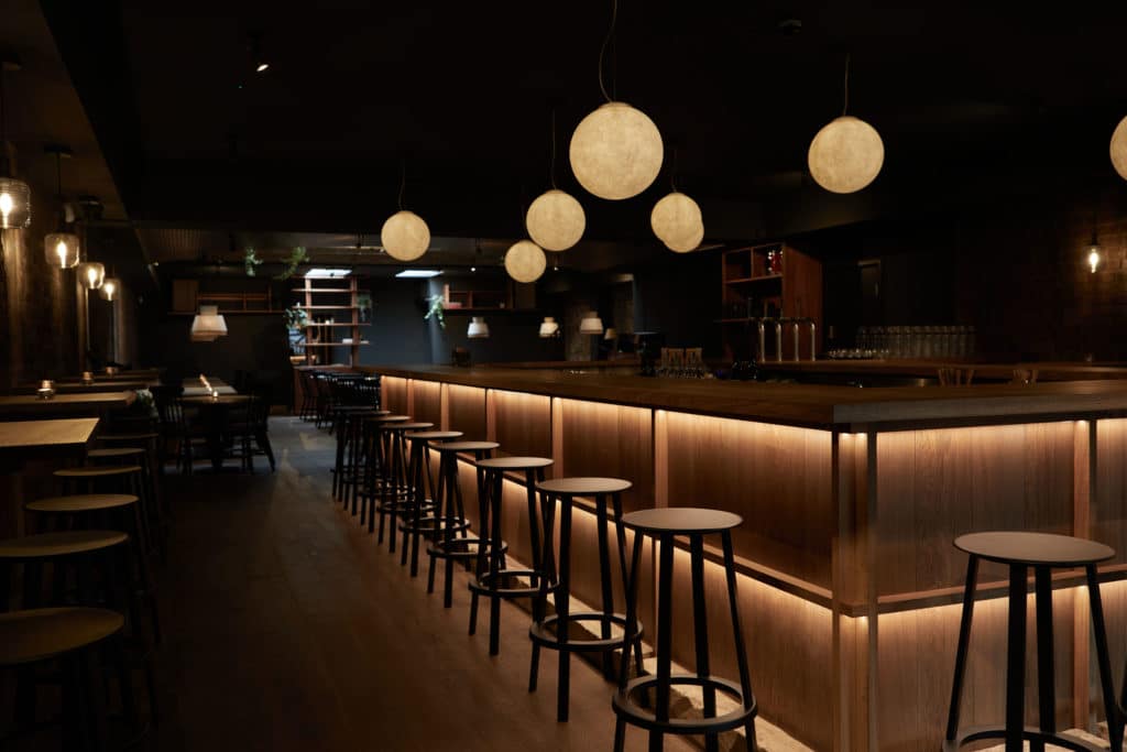 the interior of mu at night, with the underlit bar and some barstools, as well as moon-shaped light fixtures visible