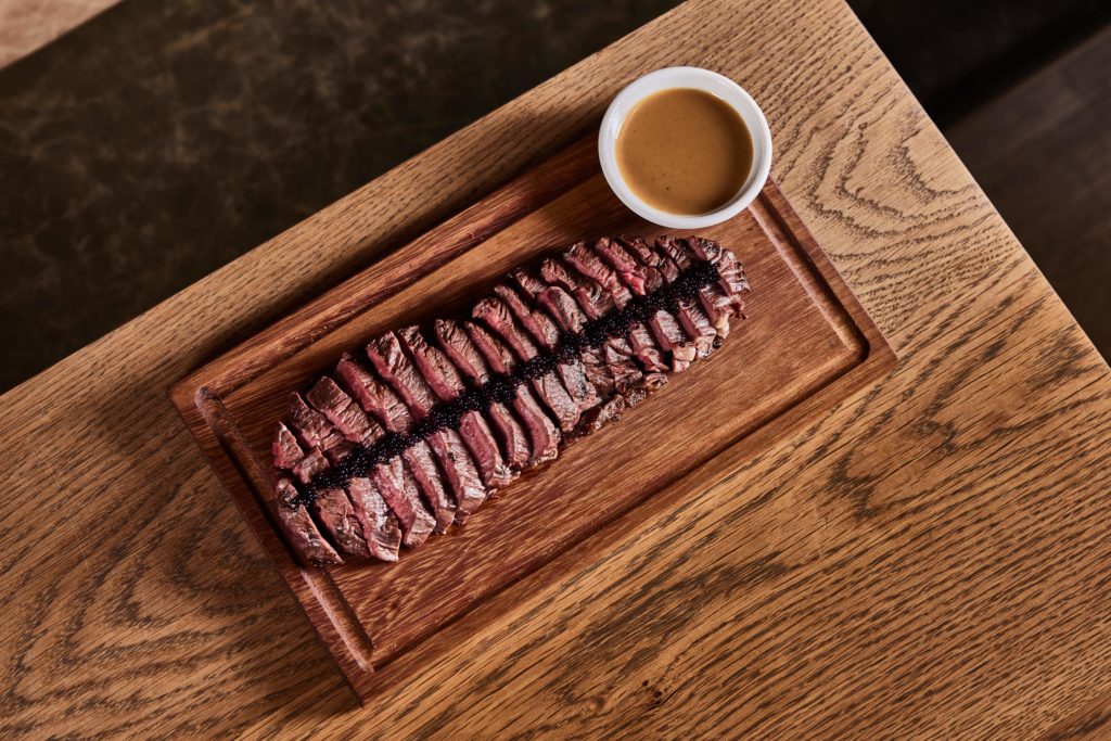 a chopping board with beef and caviar, atop a wooden table