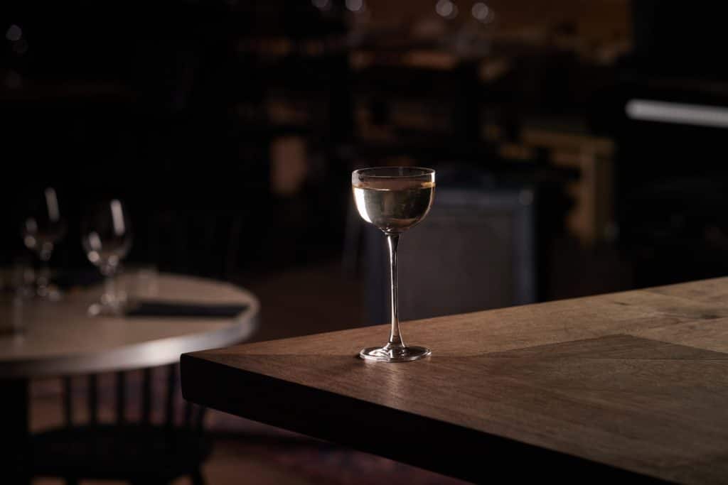 A coupe glass holding the saketini cocktail, alone on a wooden table