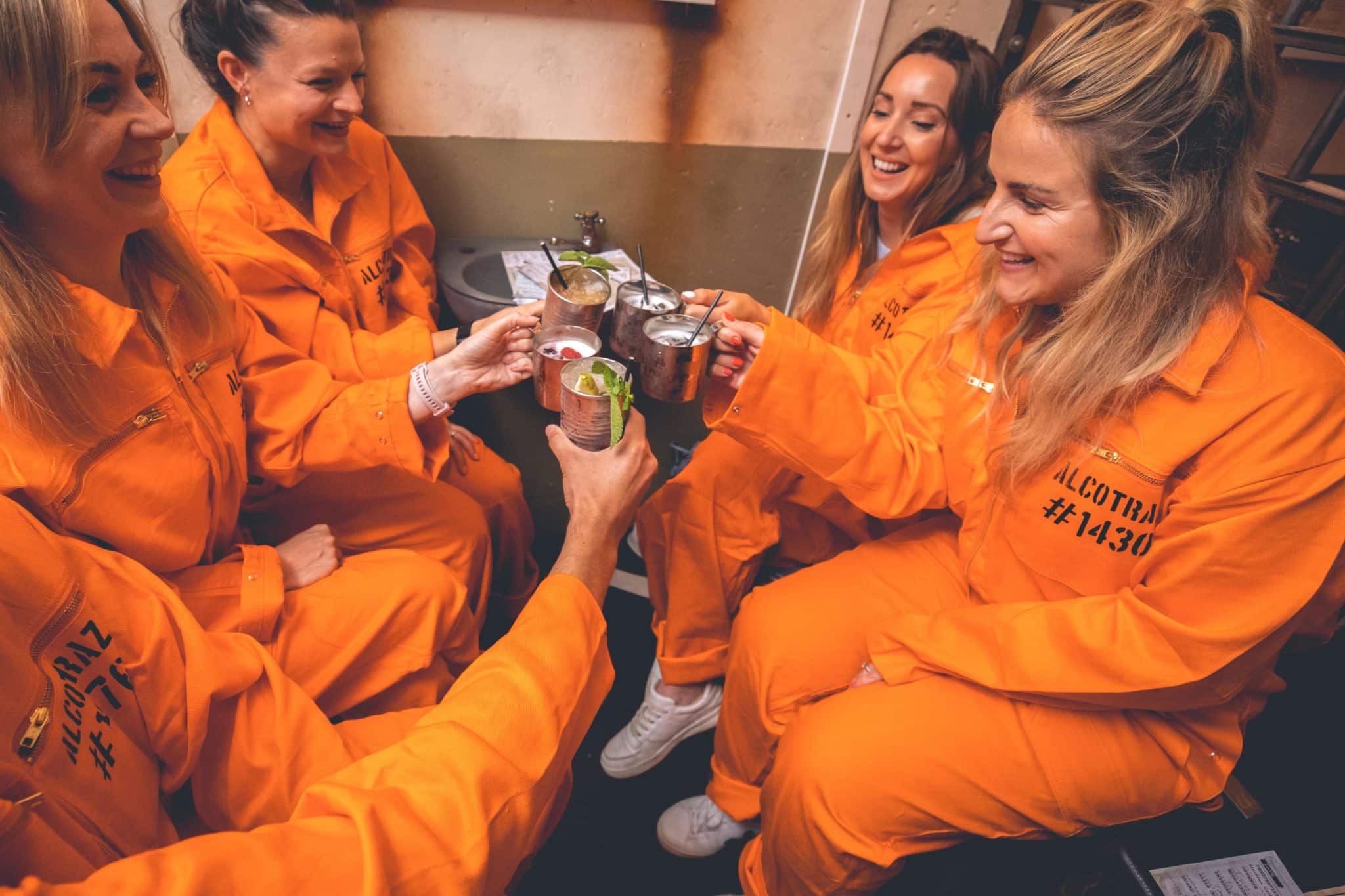 guests cheersing their drinks, wearing orange jumpsuits