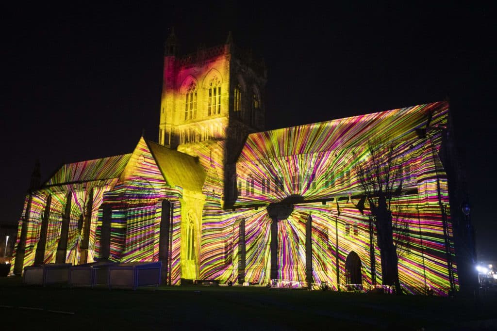 the about us lightshow on the walls of a building in Paisley, with a kaleidoscope of colour all across the building