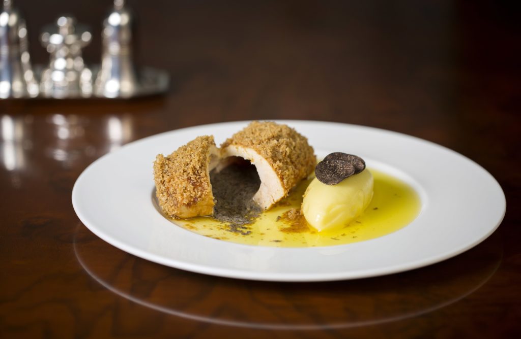 a chicken kiev, cut open, with its fillings pooling the plate, with a small mound of mashed potatoes next to it