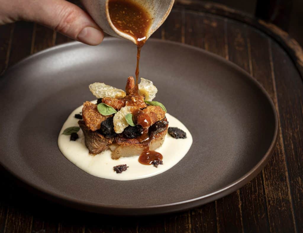 a sauce being poured over the braisedpigs head dish
