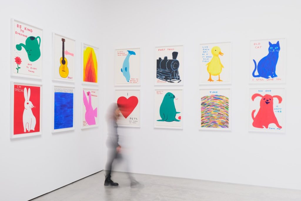 a visitor walking past a wall festooned with brightly coloured David Shrigley works