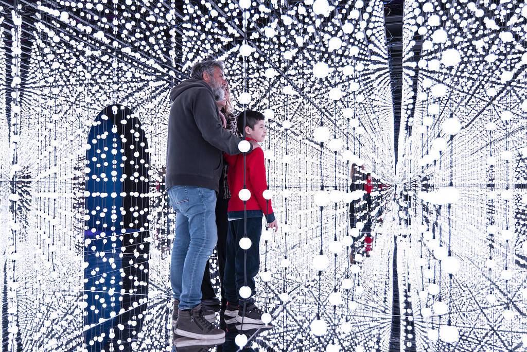 une famille de trois personnes debout au milieu de l’installation « Bubble Planet », une salle aux murs recouverts de miroirs où d’innombrables bulles suspendues les entourent