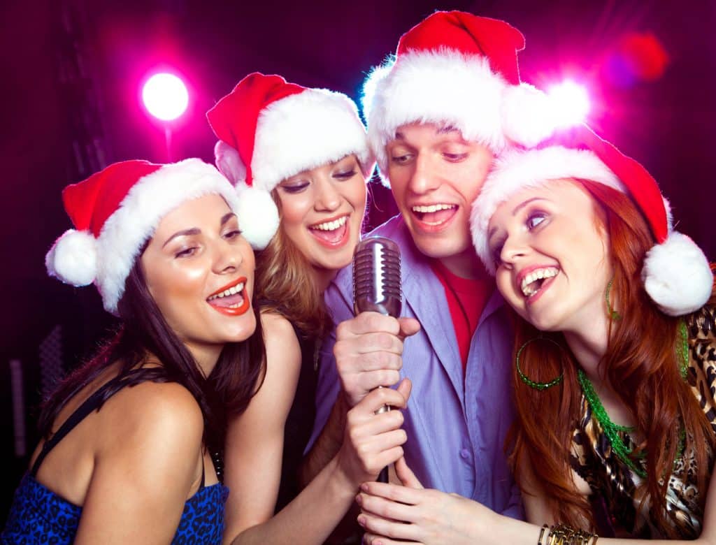 four friends in santa hats singing into one microphone