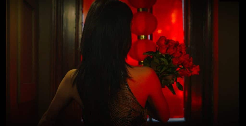 a shot of someone from behind, entering a red-lit room, holding a bouquet of flowers