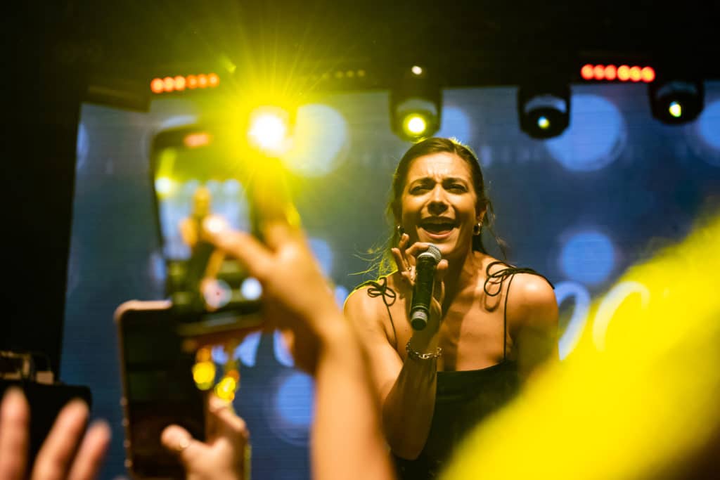 someone on stage performing as the crowd takes photos and videos on their phone