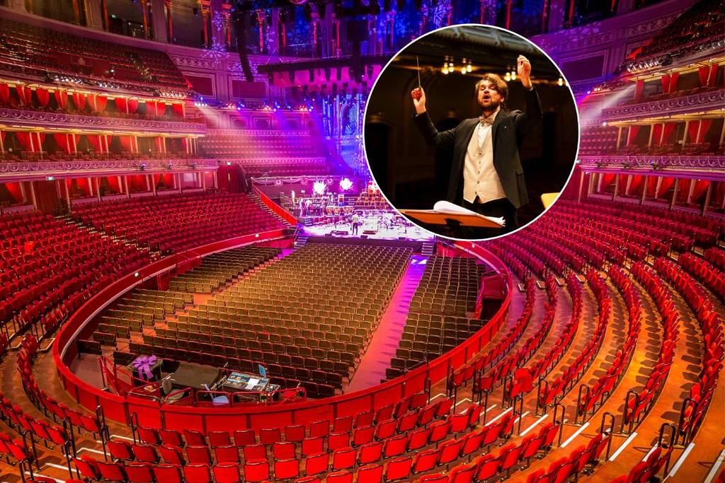 The inside of The Royal Albert Hall in London including the stage and red seating and a conductor perfoming on stage while conducting a string quartet at a classical music concert in London