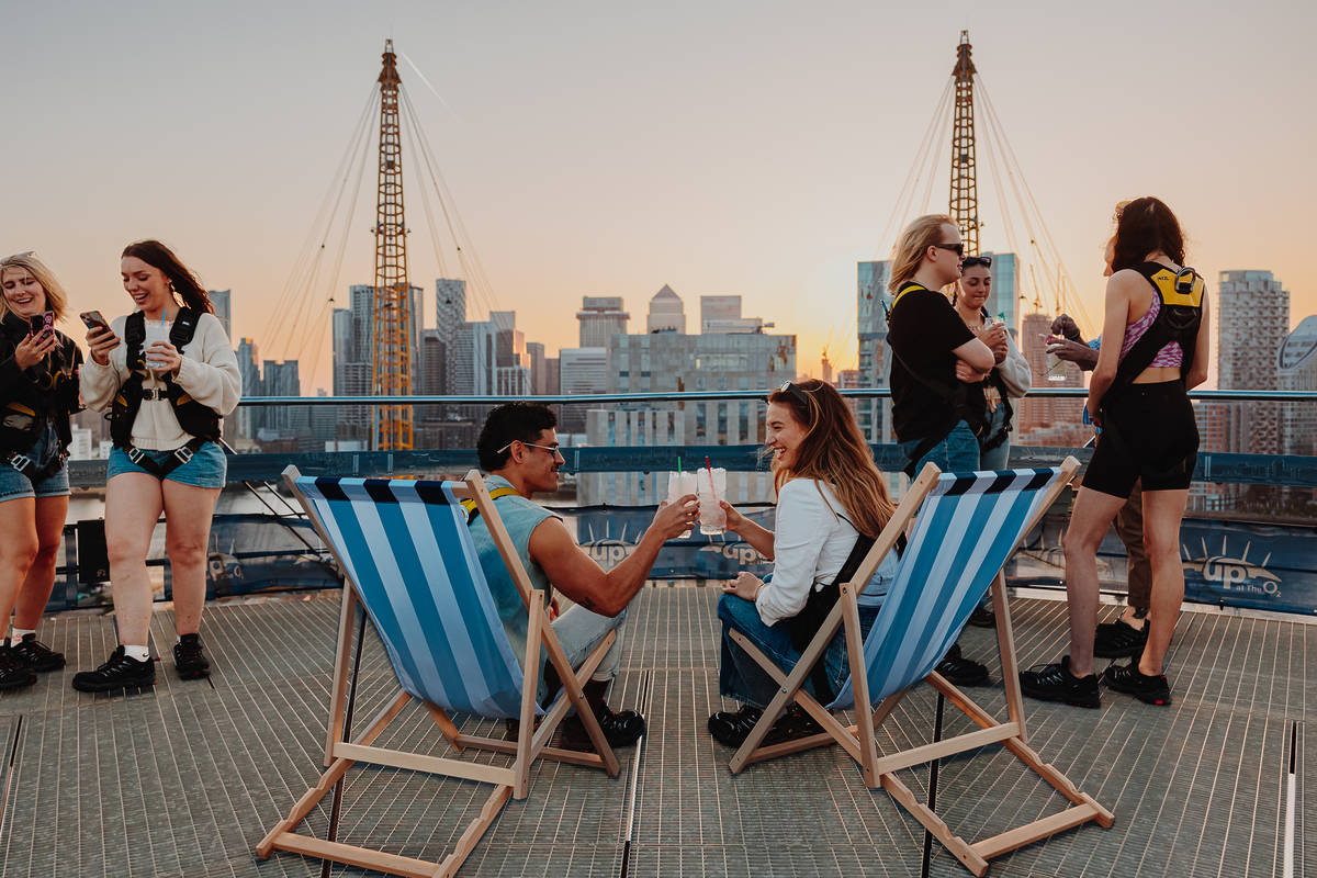 people sitting in beach chairs and standing around, enjoying cocktails atop the o2