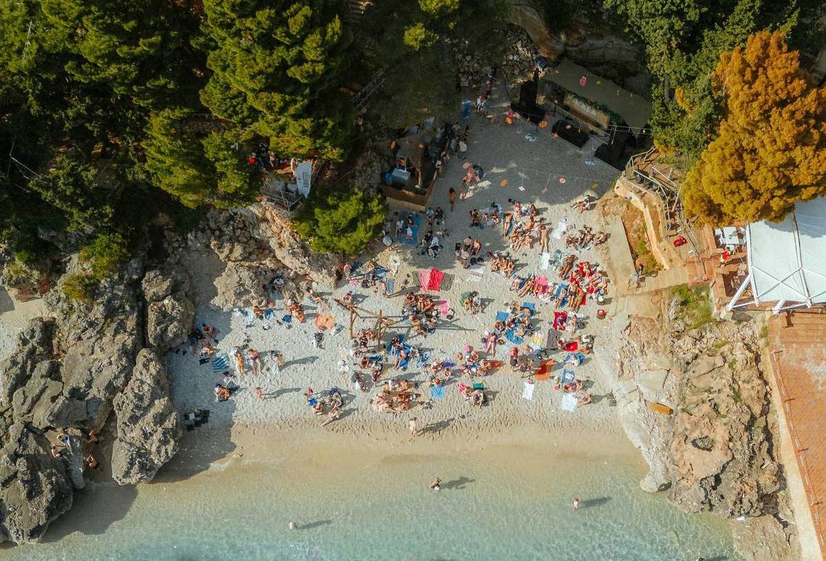 A drone shot of the beachside at Kala festival where you can see rocks, greenery and people on the beach