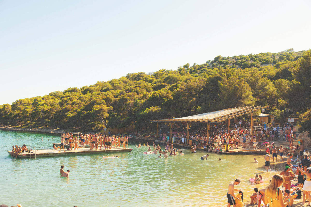 Beachside where you can see clear blue water, greenery and people partying at the beach at Love International festival