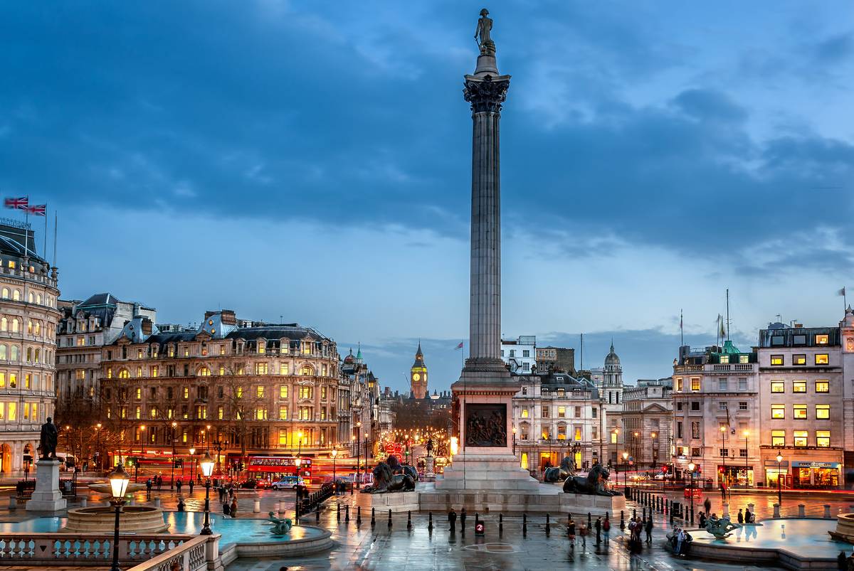 An image of the trafalgar square fountains and bright lights of traffic in the evening