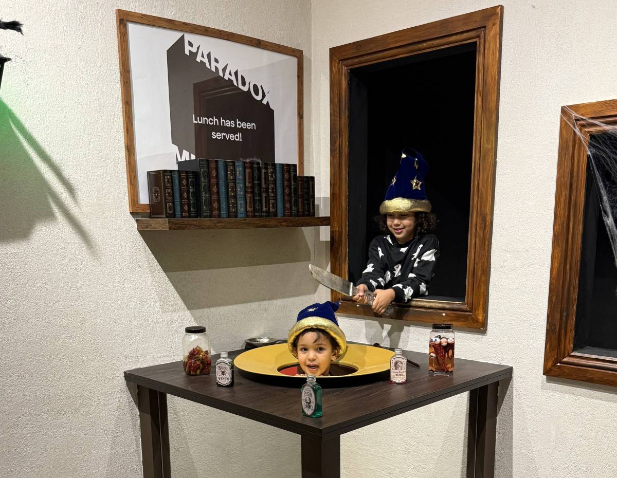 two children in ghost onesies laugh as they pose in an optical illusion where it appears like there is a head sitting on a plate at Paradox Museum London
