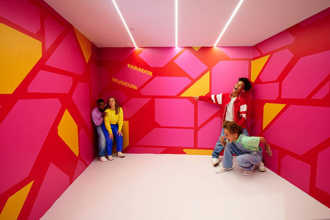 a mind-bending visual illusion in a room where two parents look much smaller than their two children, in opposing ends of the room. the children are laughing a their parents, who are pretending to look scared