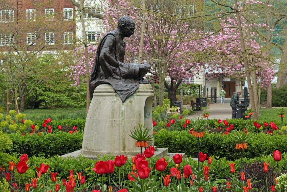 Sculpture of Mahatma Gandhi on Tavistock Square Gardens with flowers and trees in bloom.