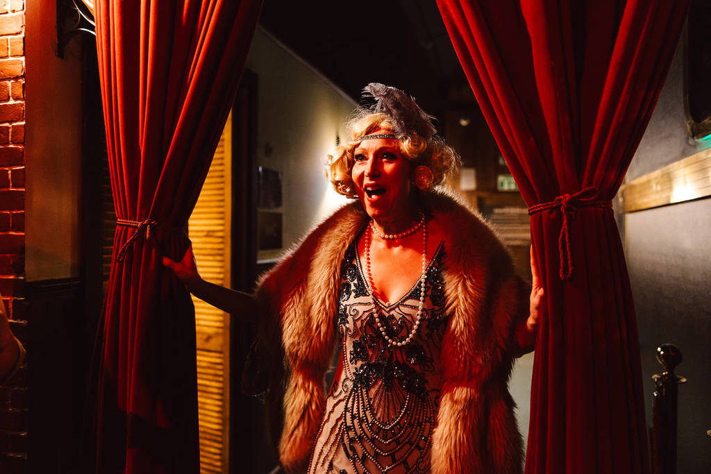 a woman dressed in a 1920s outfit bursting through red curtains at the Murder Express