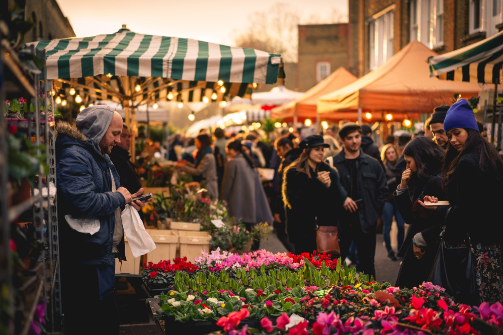Vendor checking their phone at a bustling Columbia Road Flower Market in Londno.