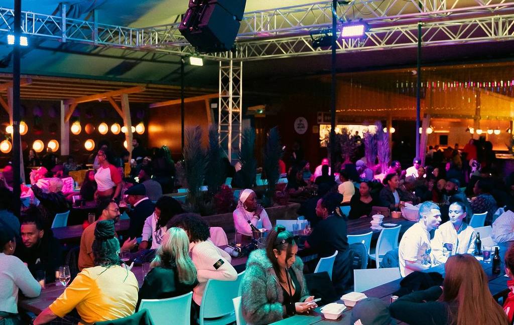 a crowd of people eat on long tables with purple lighting at Freight Brixton