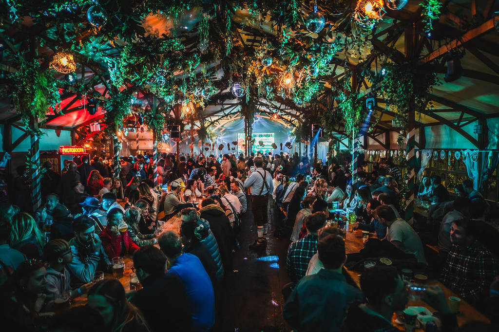 a crowd of people sit at tables under a vine-twisted roof at Between The Bridges