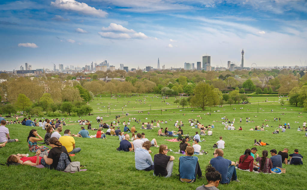 People sitting on Primrose Hill with a view of the London skyline