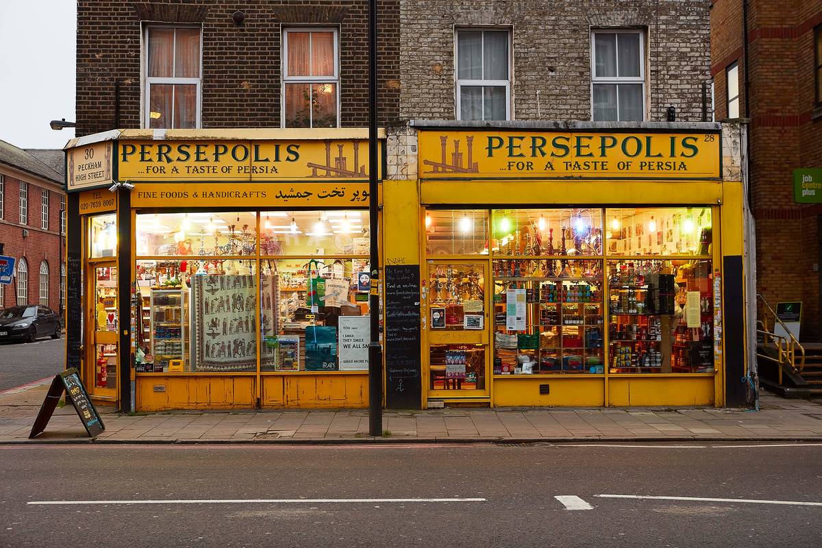 outside view of perseopolis restaurant in peckham where you can see a yellow sign and the inside of the shop lit up