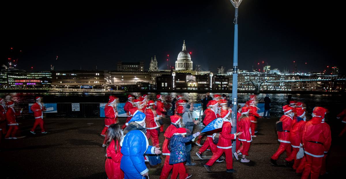 A group of people dressed as Santa running past an illuminated St Paul's Cathedral for a festive fun run
