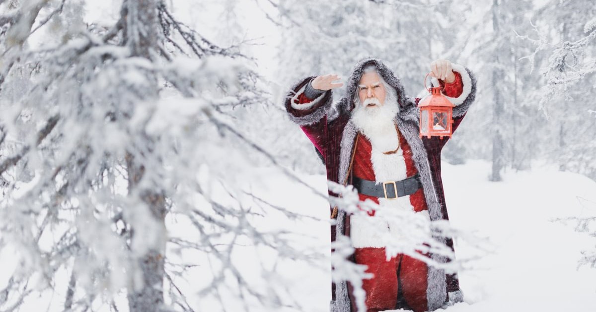 Santa Claus holding a lantern looking through a wintery woods at a lapland day trip enontekio