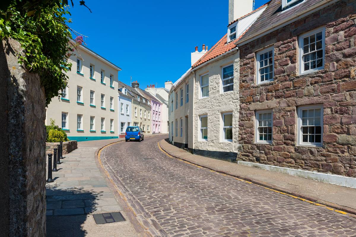 A quiet cobbled street on the island of Alderney with a single car driving down it