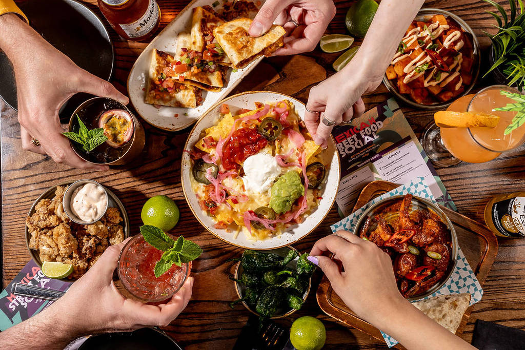 mani che si protendono per prendere cibo e bevande da un tavolo imbandito con ogni tipo di tapas e piatti da condividere