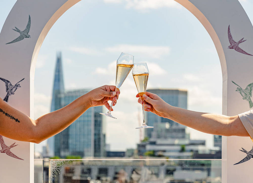 two people cheersing with Champagne glasses against a backdrop of the London skyline