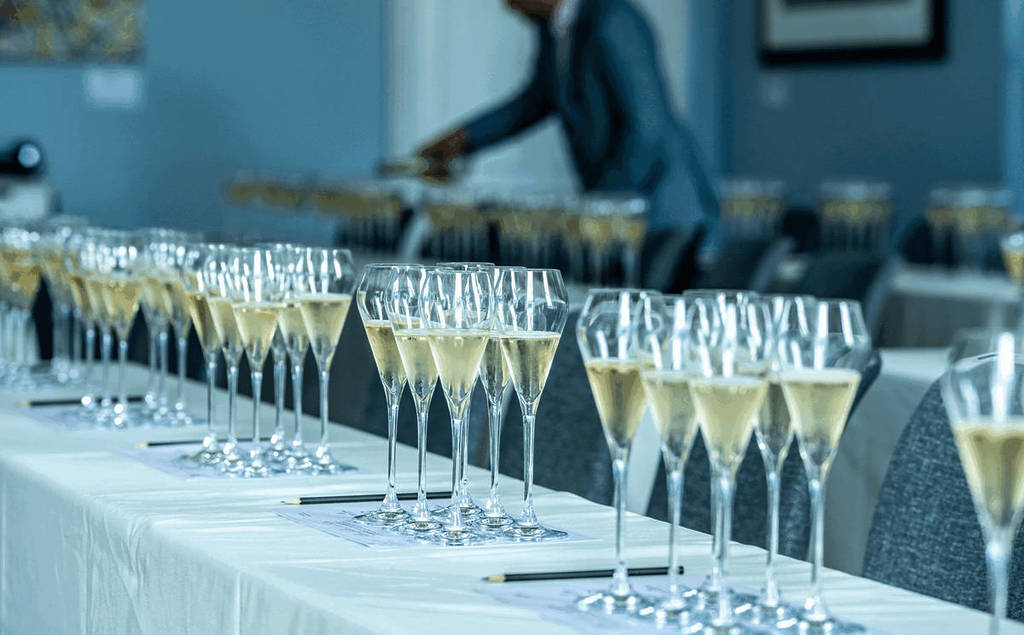 multiple table settings of six glasses of champagne, along a long white-linened table