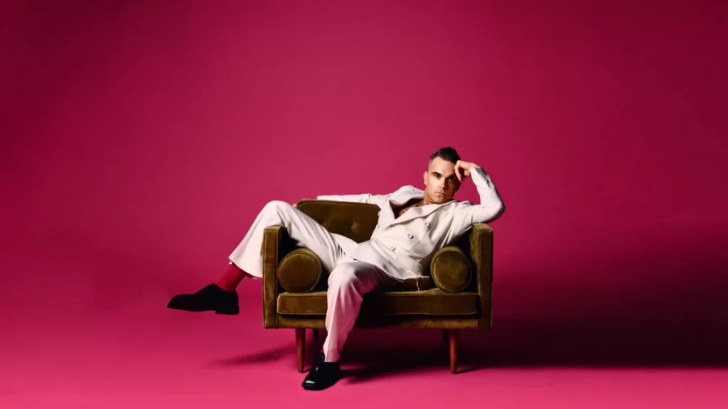 Singer Robbie Williams sprawls on a velvet sofa in a pink room
