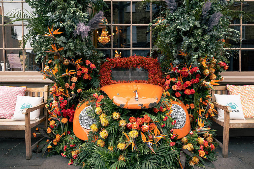 une voiture orange, entourée et remplie de fleurs orange - certaines débordant même de l'avant du capot de la voiture