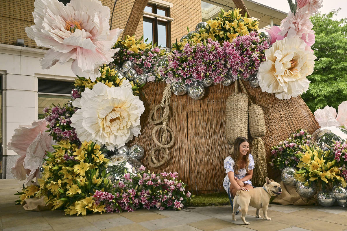 a dog and its owner posing in front of an enormous house-sized handbag made from flowers and blooms