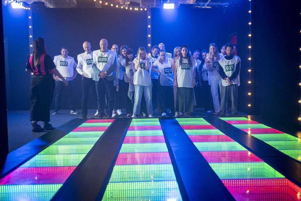 a crowd of people look scared as they prepare to take on the Memory Steps challenge at Squid Game The Experience