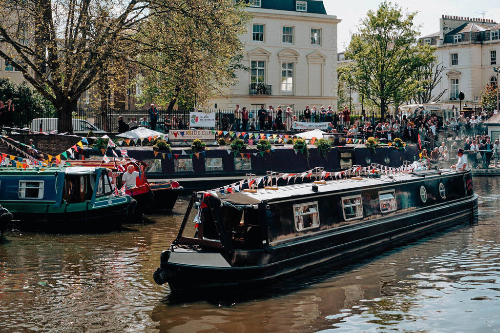 een kanaalboot die langs andere boten vaart, terwijl menigten mensen toekijken, in Little Venice