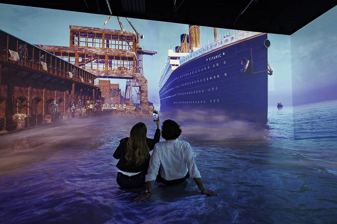 two people on the floor in front of a huge screen at a titanic experience