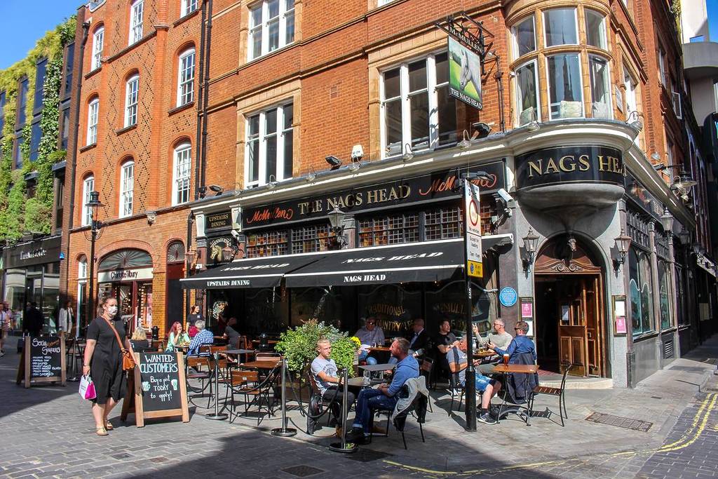 people sat at tables outside a pub on the corner of a London street