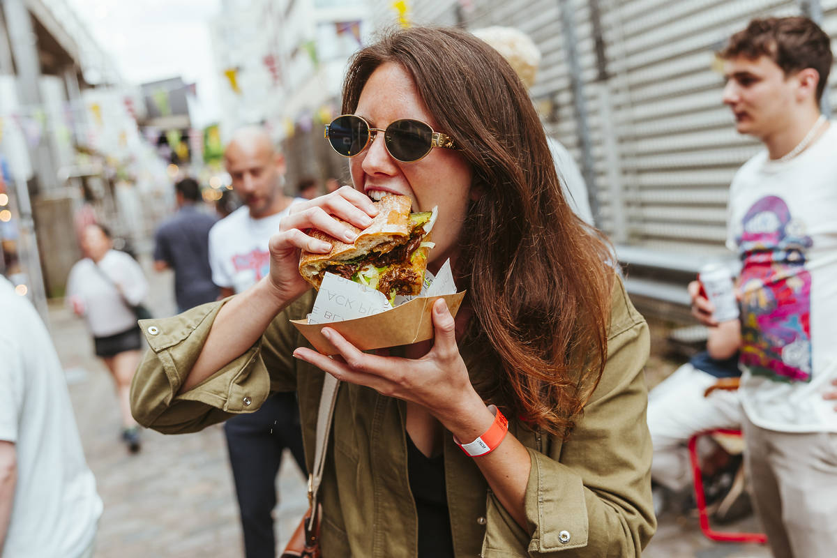someone holding a huge sandwich as they take a bite out of it